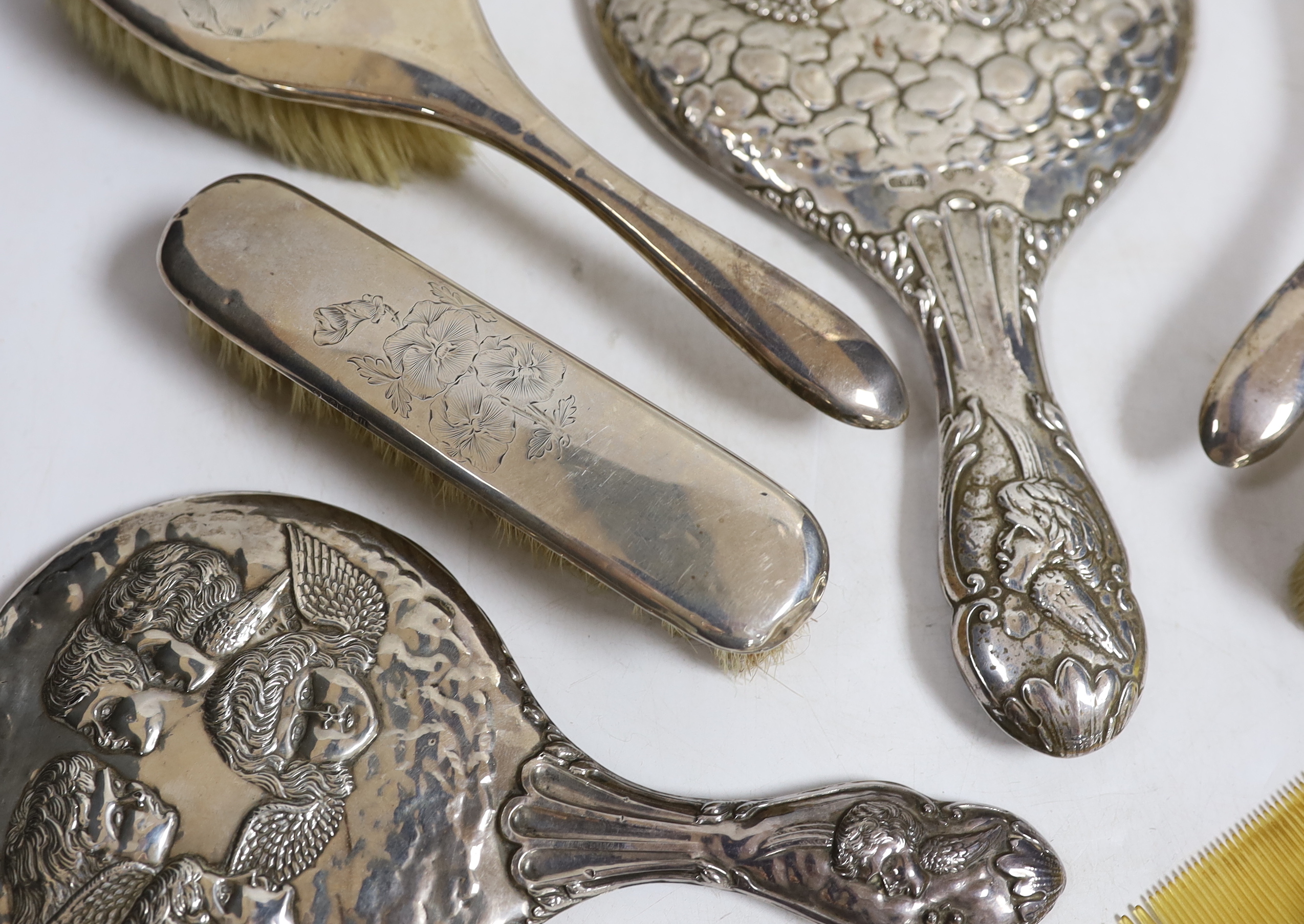 Two early 20th century repousse silver mounted hand mirrors with Reynold's Angels decoration, four silver mounted brushes and a comb.
